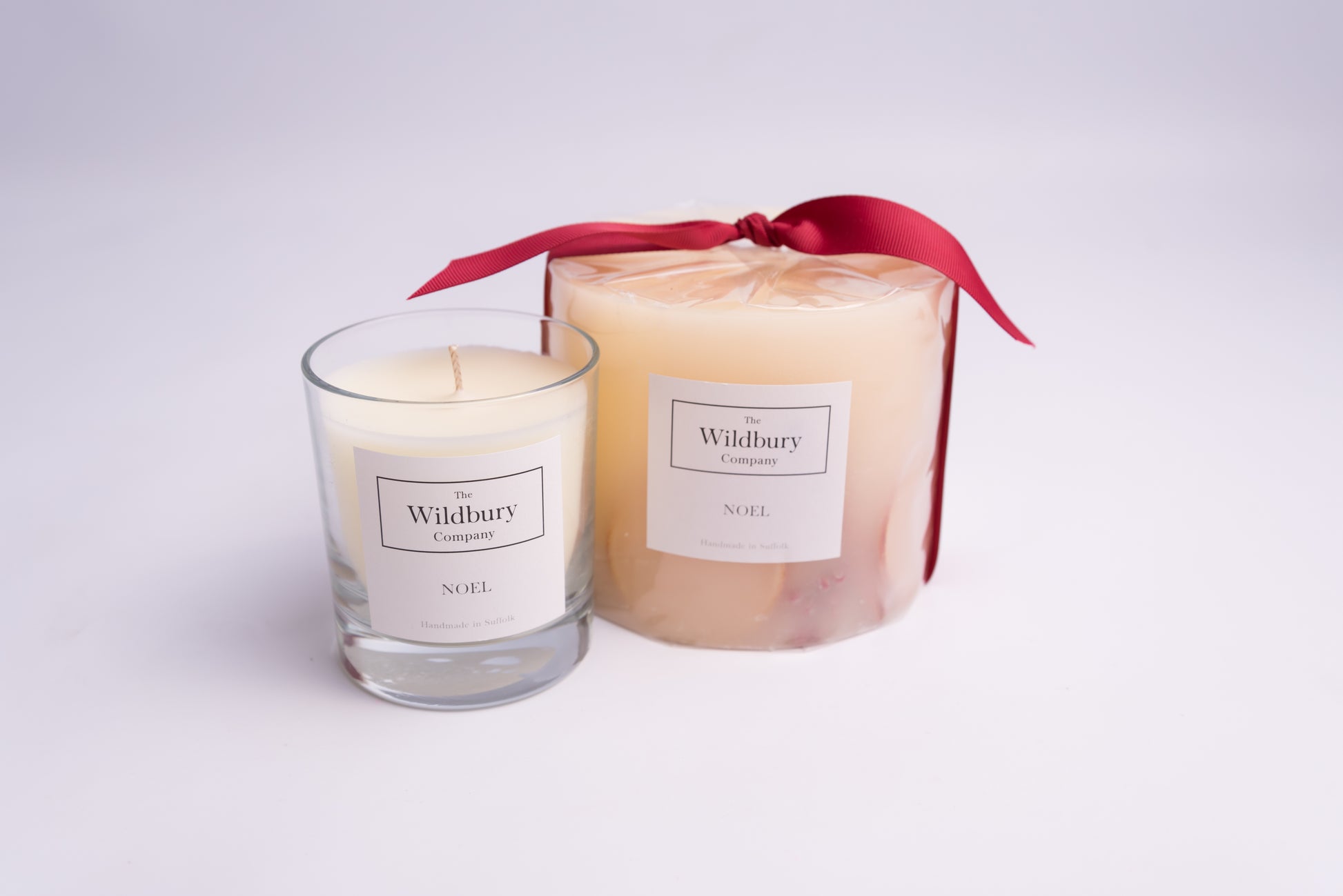Noel Candle Collection of a Large Botanical Candle with red ribbon and a smaller Signature Candle with single wick. 